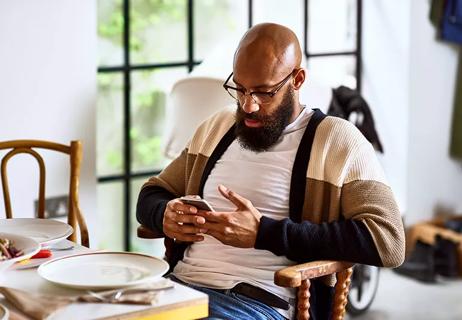 Man with no hair on the top of his head sitting at a table looking at his smartphone