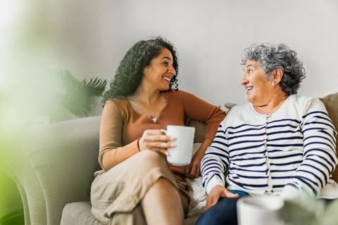 Two people sitting on couch, having coffee, laughing and chatting