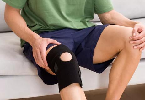 Wearing a knee brace, a man holds both his knees in discomfort or pain.