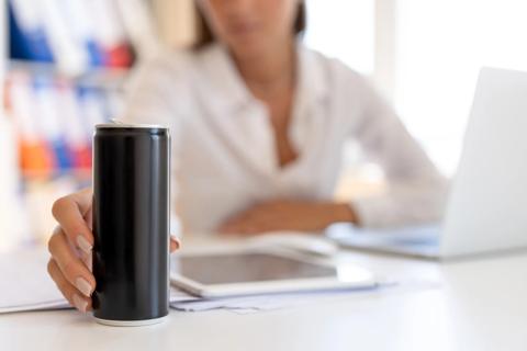 Person at work desk, hand on energy drink can