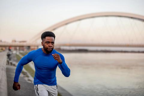 Man running intently on path outside, arched bridge nearby