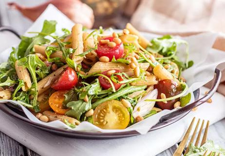 Lentil pasta salad with tomatoes and green on a metal plate atop a set table