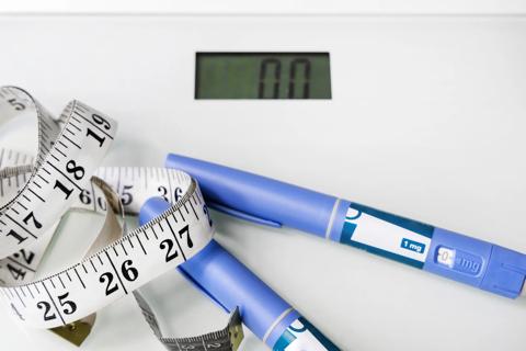 GLP-1 medication injectors on top of a scale with a tape measure.