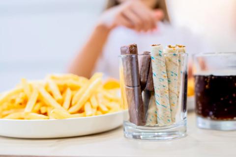 Person with salty, sweet and fatty snacks, with french fries, chocolates and soda pop