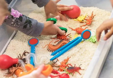 Children playing with a sensory bin filled with dried rice and toys