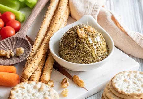 Scoop of mushroom walnut pate in a white bowl surrounded by crackers and vegetables