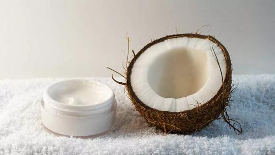 jar of coconut oil-based cream next to a cut open coconut on a bath towel