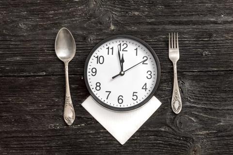 A fork and spoon alongside a clock with the time approaching 12 o'clock.