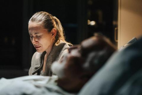 Angusihed person sitting by hospital bedside of loved one