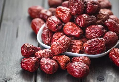 Dried Jujube fruit overflowing a white bowl on a wooden table.