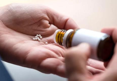 Person pouring homeopathic pills into palm of hand.