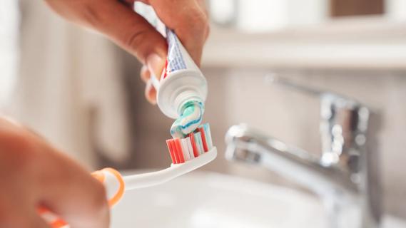 Hands squeezing toothpaste onto a toothbrush over a sink