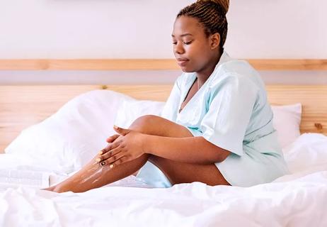 Person sitting on bed moisturizing legs after razer burn.