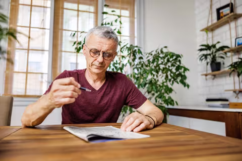 Person sitting at dining room table doing a crossword puzzle