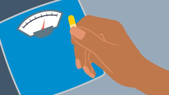 Hand holding yellow capsule in front of bathroom scale