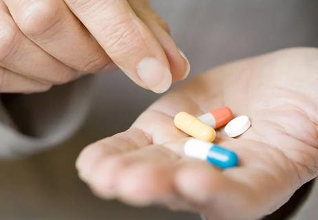 Hand holding four colorful pills as another hand hovers as if to pick one up