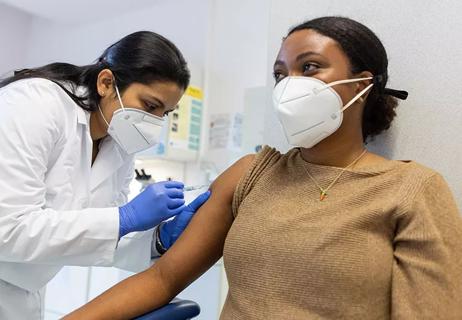 Doctor wearing PPE injecting a vaccine into a patient's arm.