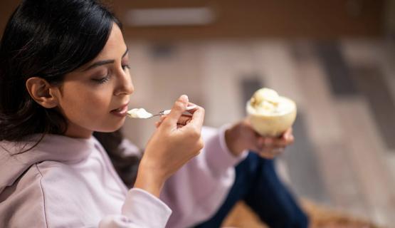 Person eating a spoonful of ice cream, holding a glass bowl of ice cream