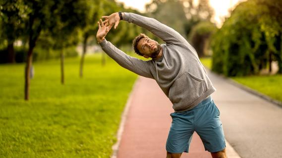 Person standing doing a side stretch on a walking path outside