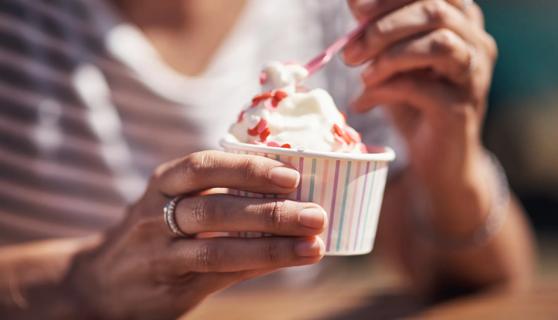 Person holding cup of ice cream, using a spoon to scoop some up