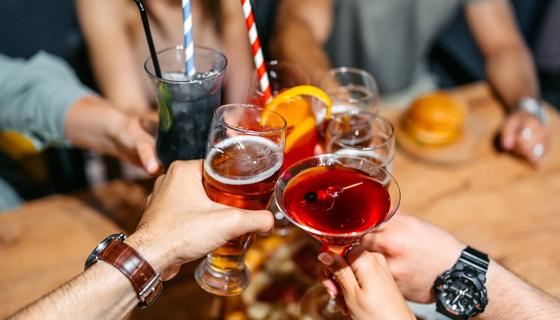 Multiple hands and a variety of glasses and drinks raised together in a toast