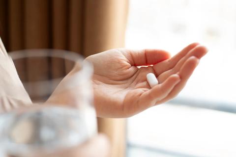 Person’s hand holding a pill, with a glass of water in the other hand