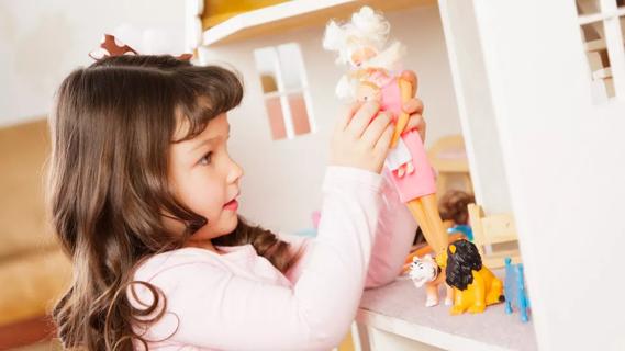 Young girl plays with a doll in a dollhouse