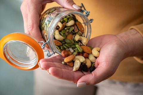 Hand holding jar of assorted nuts, pouring them into their other hand