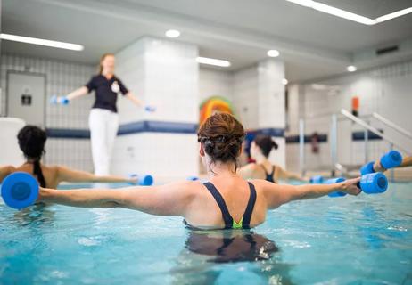 An instructor leads a water aerobics course as the students lift small dumbbells in a pool.