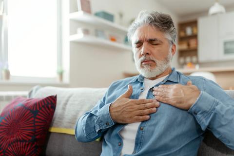 Man sitting on couch, grimacing, with both hands on chest
