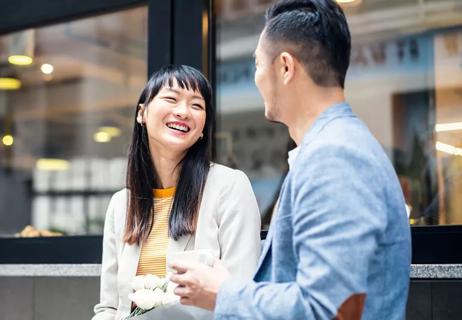 Couple sitting in front of office building laughing and flirting over coffee.