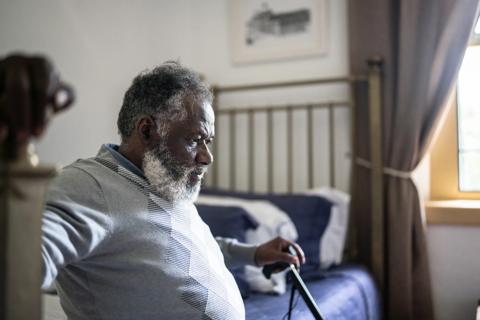 Older person with cane, sitting down on bed