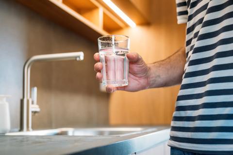 Person holding a glass of water above a sink up close