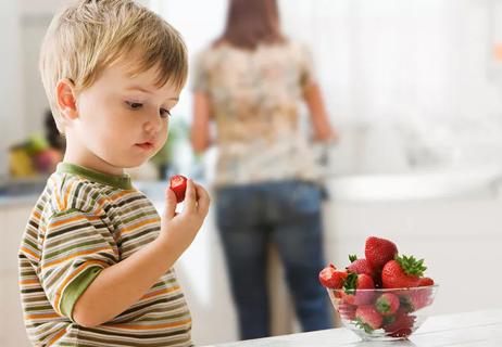 A child eating a strawberry from a bowl