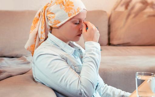 Person wearing cancer head scarf sitting with hand up to their face, feeling unwell