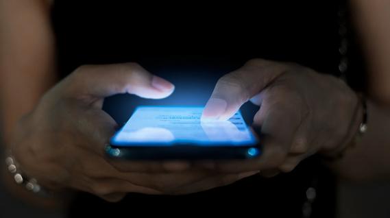 Hands holding cell phone, emitting blue light