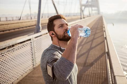 Person stopped on bridge during workout, wearing arm band and earbuds, to drink from water bottle