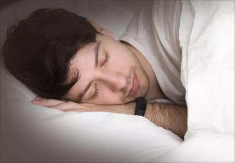 Man wearing a fitness watch on his wrist while sleeping in bed.