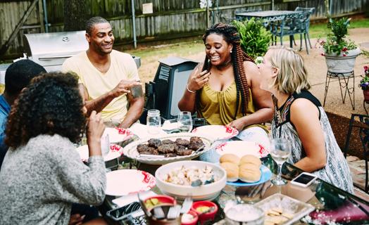 Group of happy people sitting around table full of food, having a cookout