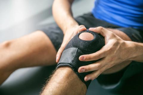 Person’s hands holding their knee with a knee brace on it