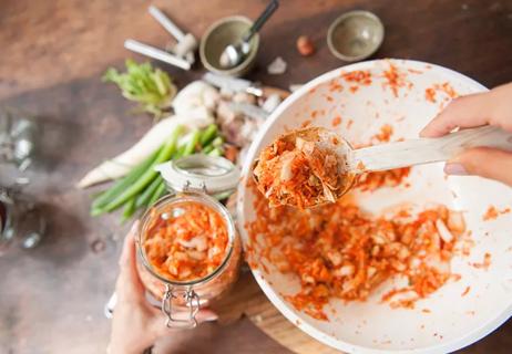 A person sifts through a food mixture containing chopped up carrots, shallots and other vegetables