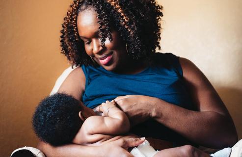 Smiling mother looking down on baby breastfeeding