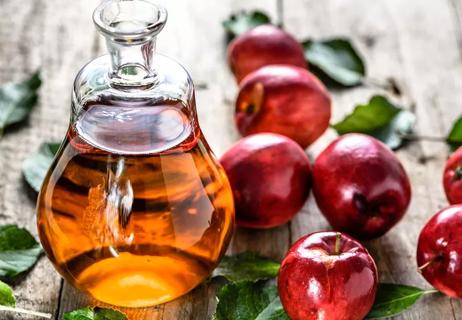 apple cider vinegar in a stoppered glass caraf with apples in background on wooden table.