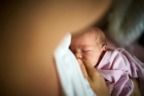 Newborn baby in pink shirt is nursing with caregiver