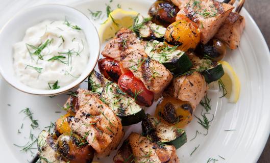 Grilled salmon chunks and veggies on skewers, with creamy dill yogurt sauce on the side