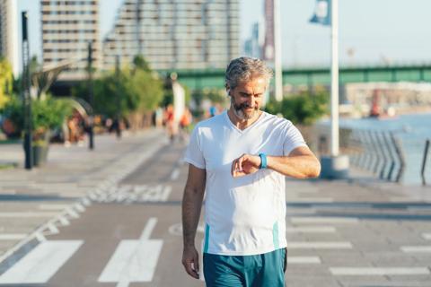 Smiling man walking on paved path outside, looking at smartwatch