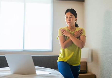 person stretching with arms crossed over chest and looking a laptop screen