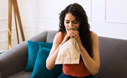 Person sitting on couch, breathing into a paper bag