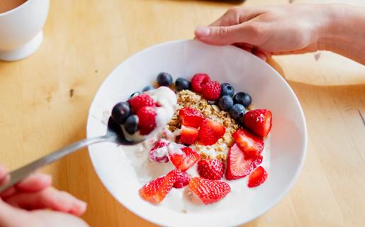 Hand scooping up spoonful of yogurt, granola and fruit from bowl