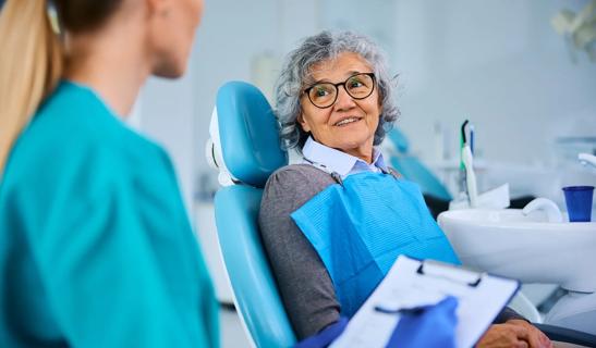 Person sitting in dental exam chair, speaking with dental provider